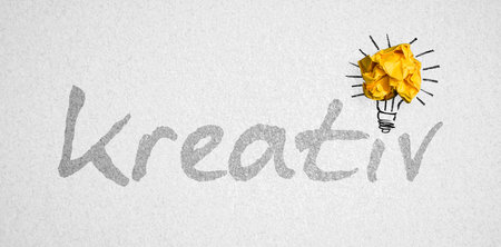 German message for CREATIVE and crumpled paper forming a lightbulb symbol on paper background