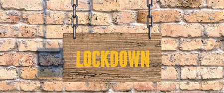 wooden sign on chains with message LOCKDOWN in front of a brick wall - 3d illustrationの写真素材
