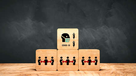 stack of cubes with social distancing, face mask and syringe symbols and the text COVID-19 in front...