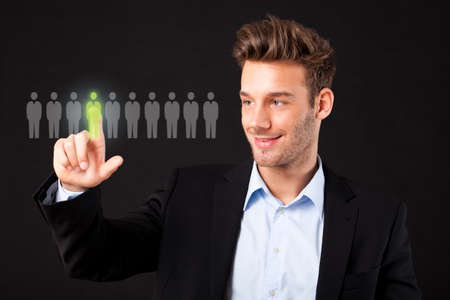 businessman selecting a person out of a group on a virtual screen in front of black backgroundの写真素材