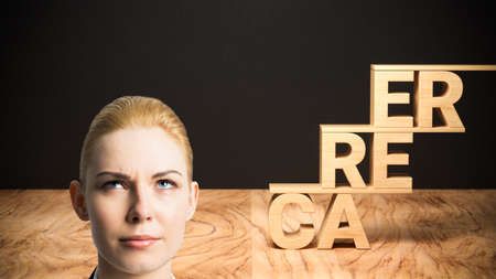 businesswoman thinking about her career visualized by the word CAREER formed as a stair in front of a blackboardの写真素材