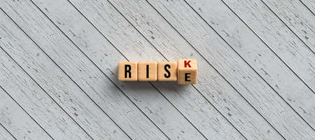 Risk versus Rise concept with revolving alphabet letters on wooden cubes over a diagonal grey wood plank background with copyspace in a panorama banner - 3d illustrationの写真素材