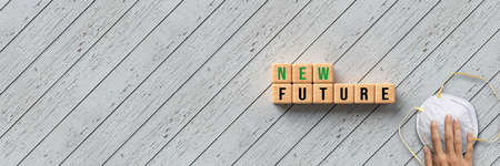 New Future of New Normal concept for the  pandemic with text on wooden blocks and a female hand reaching for a protective face mask over a grey diagonal wood background with panorama copyspaceの写真素材