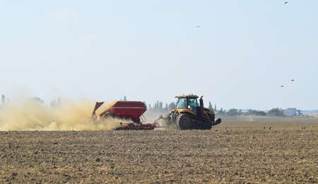 Russia, Temryuk - 19 July 2015: Tractor rides on the field and makes the fertilizer into the soil. Clouds of dust from the dry soil tractor trailer. Fertilizers after plowing the field.のeditorial素材