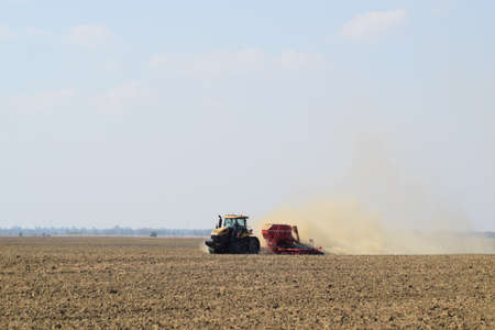 Russia, Temryuk - 19 July 2015: Tractor rides on the field and makes the fertilizer into the soil. Clouds of dust from the dry soil tractor trailer. Fertilizers after plowing the field.のeditorial素材