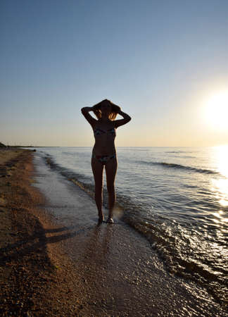 Silhouette of a girl against the sunset by the sea. The dark silhouette against the sea sunset. Girl on the beach in the evening.の写真素材