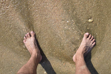 Legs men on the sea sand near sea wave. Walk on the beach.の写真素材