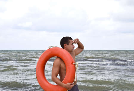 The man on the beach with a lifebuoy. Safety beach holiday at sea. Man with a life buoy on the beach. Rescue and safety on the water.の写真素材