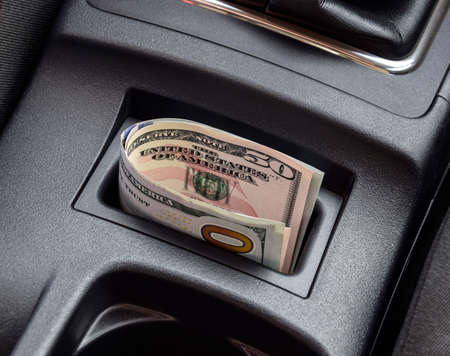 Several banknotes American dollars lie in the niche of the central console of the car. The money in the car.の写真素材