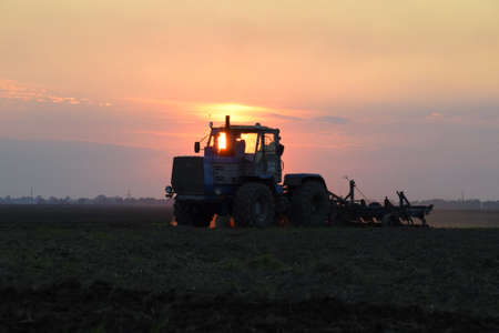 Tractor plowing plow the field on a background sunset. tractor silhouette on sunset background.の写真素材