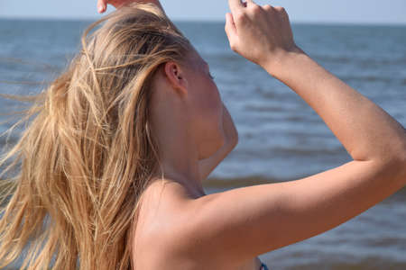 Blond girl in a bikini on the beach. Beautiful young woman in a colorful bikini on sea background.の写真素材
