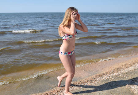 Blond girl in a bikini on the beach. Beautiful young woman in a colorful bikini on sea background.の写真素材