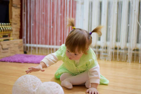 One year old baby girl sitting on the floor. A child playing with wicker balls. A blonde girl.