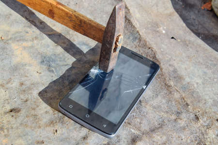 Hammer and smartphone. The screen of the smartphone, a broken hammer. The destruction of the phone.の写真素材