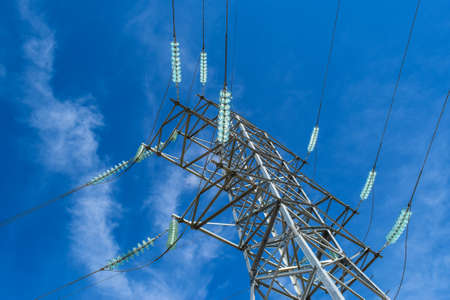Supports high-voltage power lines against the blue sky with clouds. Electrical industry.
