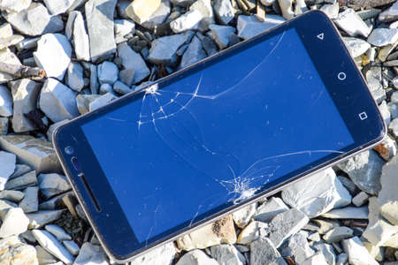Frustrated phone on the rocks. Glass shattered on rocks on a smartphone. Smartphone fell and crashed.の写真素材