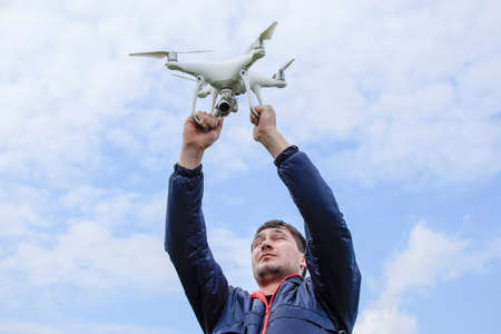 A man with a quadrocopter in his arms raised to the sky. A white drone is being prepared for the...
