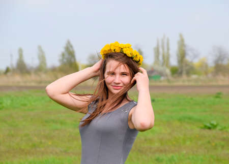 A girl with a wreath of dandelions on her head. Beautiful fairy young girl in a field among the flowers of tulips. Portrait of a girl on a background of red flowers and a green field. Field of tulips.の写真素材