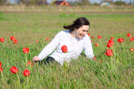 Beautiful fairy young girl in a field among the flowers of tulips. Portrait of a girl on a background of red flowers and a green field. Field of tulips.の写真素材