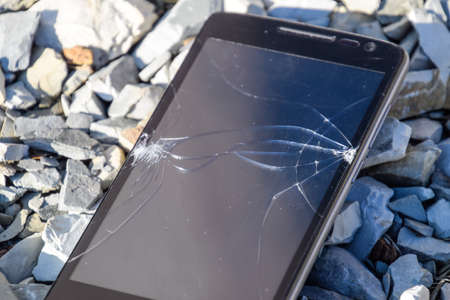 Frustrated phone on the rocks. Glass shattered on rocks on a smartphone. Smartphone fell and crashed.の写真素材