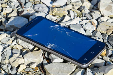 Frustrated phone on the rocks. Glass shattered on rocks on a smartphone. Smartphone fell and crashed.の写真素材