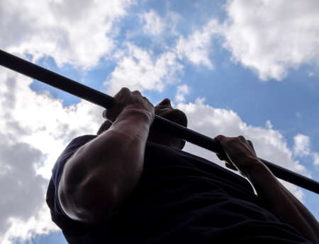 The man pulls himself up on the bar. Playing sports in the fresh air. Horizontal barの写真素材