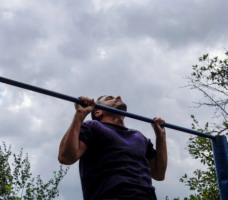 The man pulls himself up on the bar. Playing sports in the fresh air. Horizontal bar