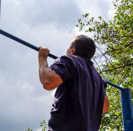 The man pulls himself up on the bar. Playing sports in the fresh air. Horizontal bar