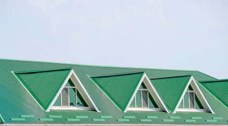The house with plastic windows and a green roof of corrugated sheet. Roofing of metal profile wavy shape on the house with plastic windows. Green roof of corrugated metal profile and plastic windows.の写真素材