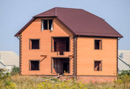 The house with plastic windows and a roof of corrugated sheet. Roofing of metal profile wavy shape on the house with plastic windows.の写真素材