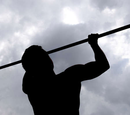 Silhouette of an athlete on a bar. The man pulls himself up on the bar. Playing sports in the fresh air. Horizontal barの写真素材