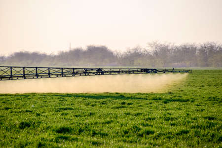 Tractor with high wheels is making fertilizer on young wheat. The use of finely dispersed spray chemicals. Tractor on the sunset background.の写真素材