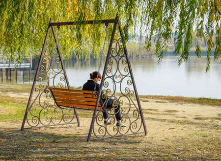 Woman is sitting on a swing. Lonely middle-aged woman on a swingの写真素材