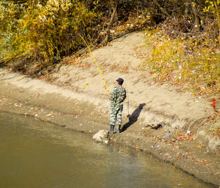 Fishermen on the bank of the river in autumn. Fishing the bait. Autumn scenery on the river.の写真素材