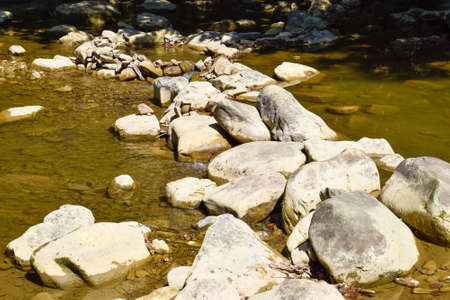 The mountain river. Shallow mountain river, water flows through the rocks. Rocks in the river water. Stones and layers of sedimentary rocksの写真素材