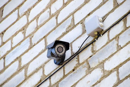 video camera with illumination is hanging on the wall. Wall of white brick and a video camera with wiresの写真素材