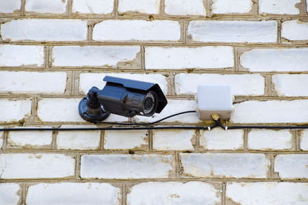 video camera with illumination is hanging on the wall. Wall of white brick and a video camera with...