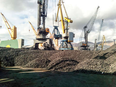 Heap of coal anthracite in the port. Port cranes for coal loading.