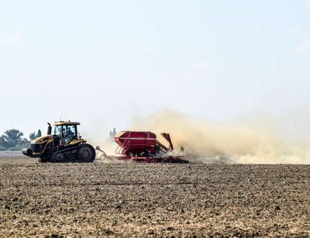 Russia, Temryuk - 19 July 2015: Tractor rides on the field and makes the fertilizer into the soil. Clouds of dust from the dry soil tractor trailer. Fertilizers after plowing the field.のeditorial素材