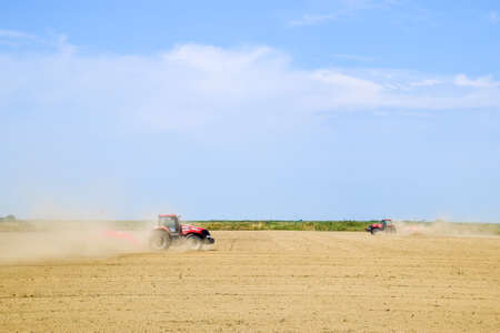 Field next to Krasnodar, Russia - August 08, 2016: A tractor with a grader aligns the soil on the field. The tractor raised dust.のeditorial素材