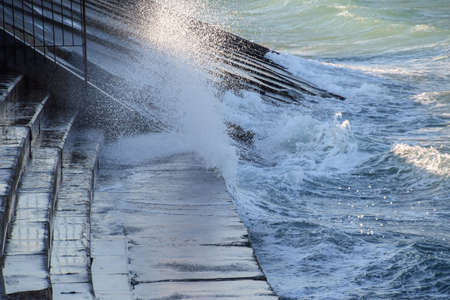 Splashes of waves on the concrete beachfront promenade. Stone steps to the sea.の写真素材