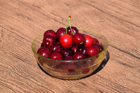Berries of a sweet cherry in a glass bowl on a wooden background. Ripe red sweet cherry.