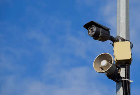 CCTV camera and loudspeaker alarm on a pole against a blue sky