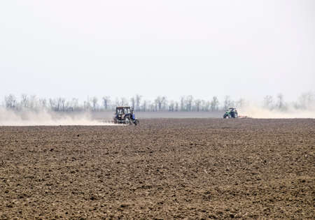 The tractor harrows the soil on the field and creates a cloud of dust behind it.の写真素材
