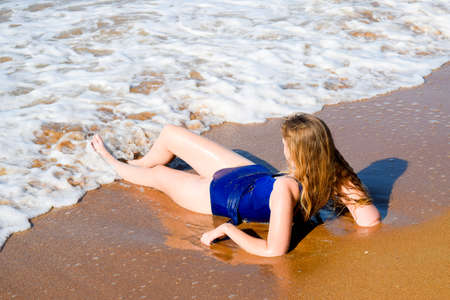 Girl in a blue bathing suit lies on the seashore and relaxes. Waves caress the girl's body.