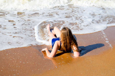 Girl in a blue bathing suit lies on the seashore and relaxes. Waves caress the girl's body.の写真素材