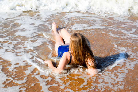 Girl in a blue bathing suit lies on the seashore and relaxes. Waves caress the girl's body.の写真素材