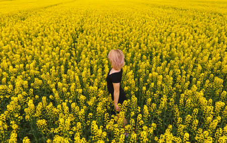 A girl in a black dress among the colors of rape in the field. Walk the girl among the yellow flowers. Flowering rape.の写真素材