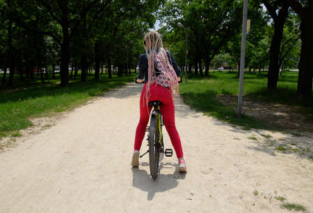 Slavyansk-on-Kuban, Russia - May 15, 2018: Young woman with a yellow mountain bike on a path in a park. A walk on a bicycle in the park. Girl with pigtails from threads.のeditorial素材