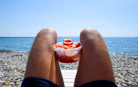 Peaches on the knees. Peeled peaches in a cup on male hairy legs. Beach vacation by the sea.